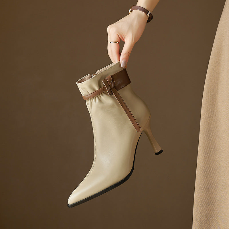 Beige ankle boot with brown strap held by a hand against a brown background