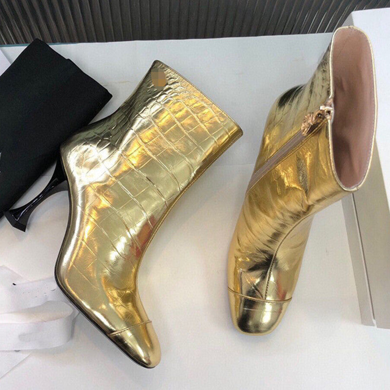 Gold metallic ankle boots on a white surface with a black bag.