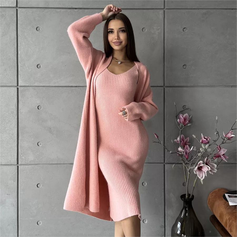 Woman wearing a pink ribbed dress against a gray tiled wall with a vase of flowers.
