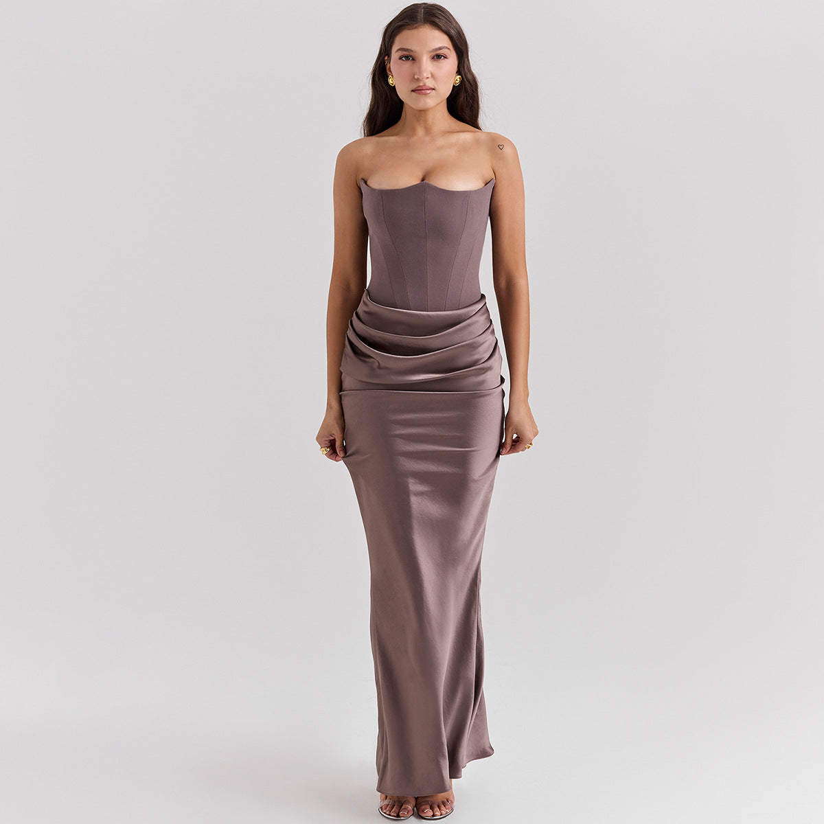 Woman wearing a strapless, floor-length dress on a plain background