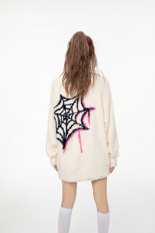 Person wearing a cream-colored sweater with a spider web design on the back against a white background