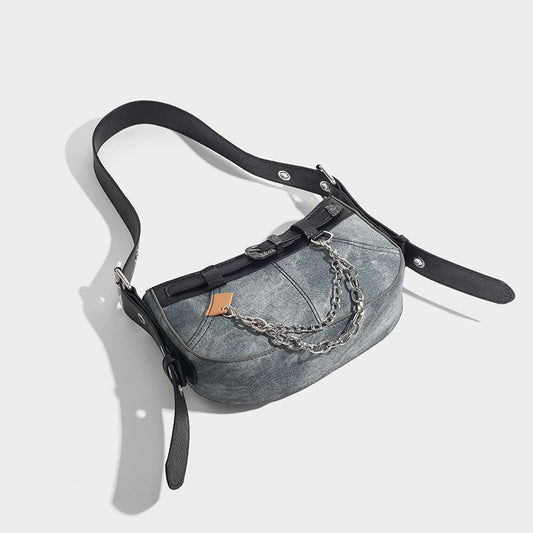 Gray denim bag with black leather straps and chain detail on a light gray background