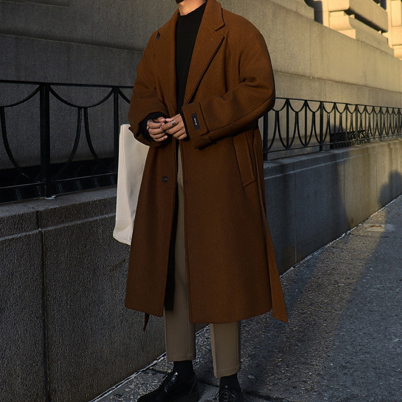 Person wearing a brown coat standing on a sidewalk with a building in the background