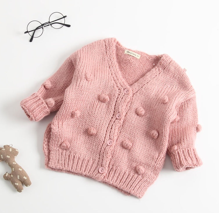 Pink knitted cardigan with pom-poms on a white background