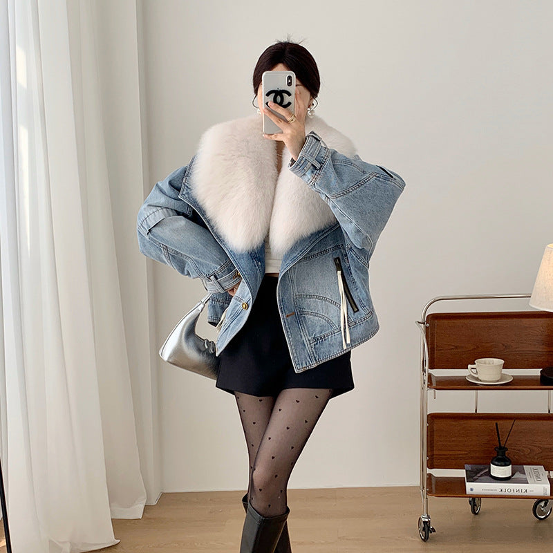 Person wearing a denim jacket with fur lining, taking a mirror selfie in a room.