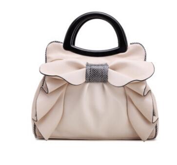 Beige handbag with a large bow and black handle on a white background