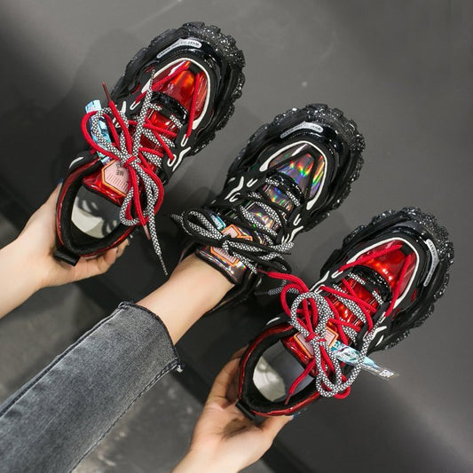 Black and red sneakers with multicolor laces held by a person against a dark background