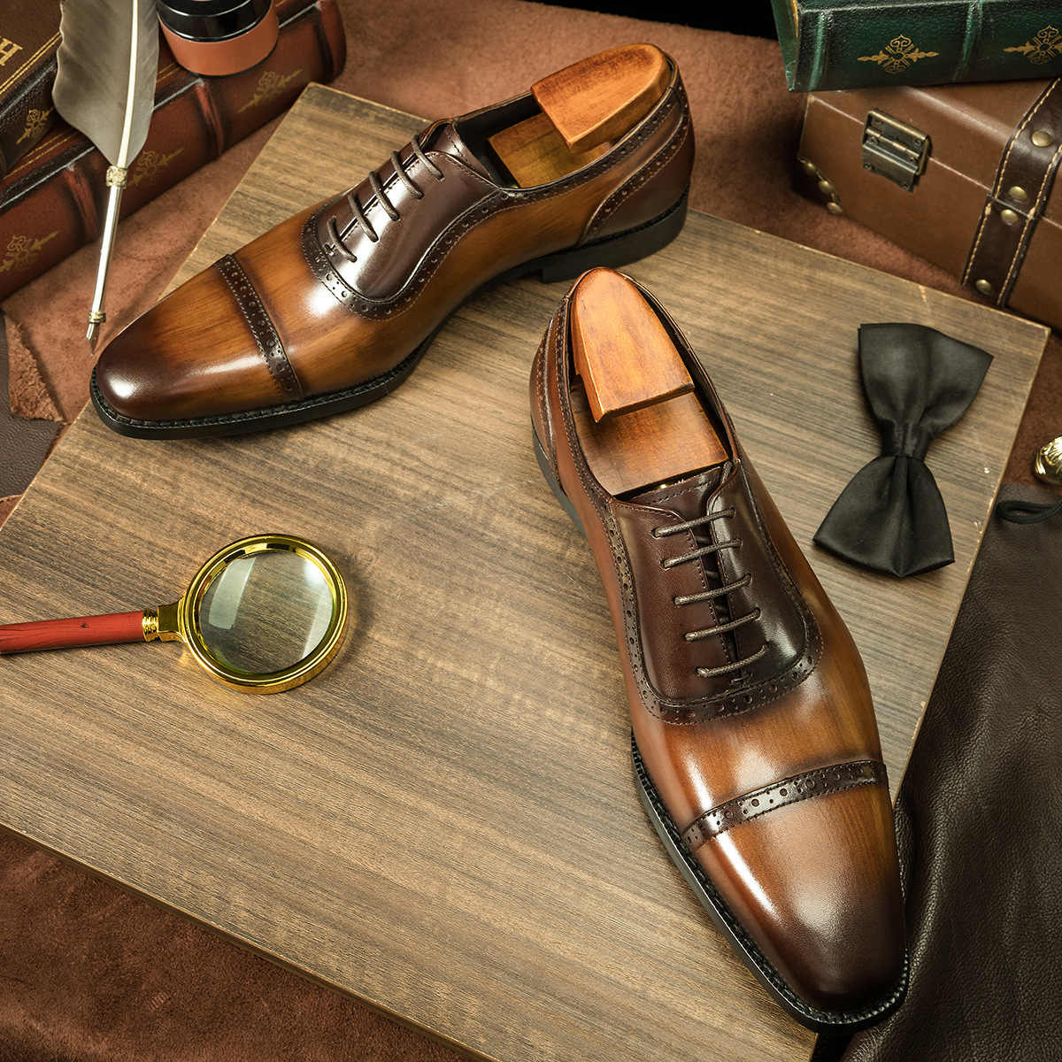 Brown dress shoes on a wooden surface with a magnifying glass, bow tie, and other accessories.