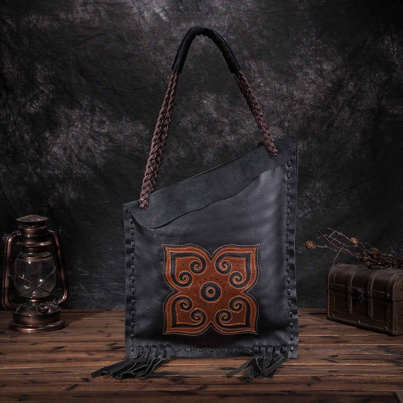 Black leather handbag with intricate brown design on a dark background