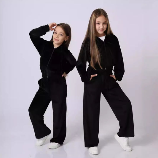 Two young girls wearing matching black outfits against a white background