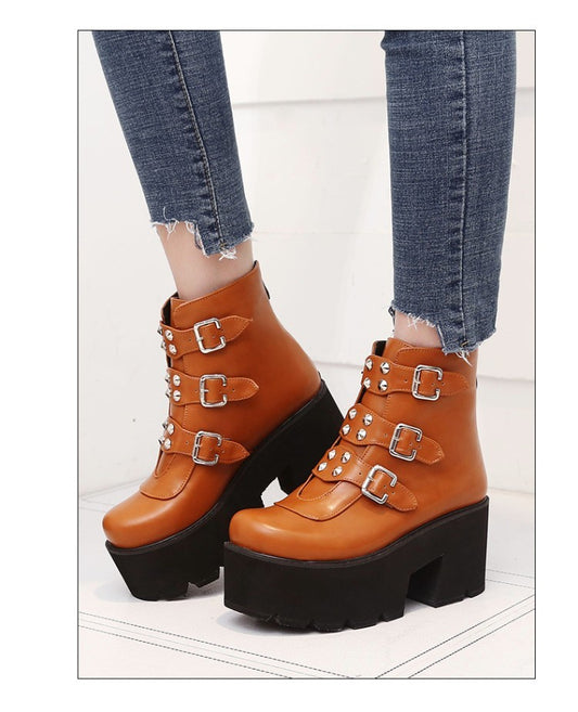 Brown platform boots with buckles worn with blue jeans on a white floor.