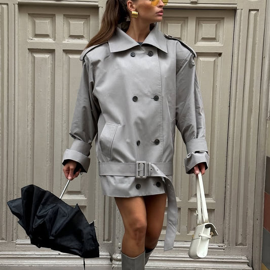 Woman in a gray trench coat holding an umbrella and a handbag against a neutral background by millivan