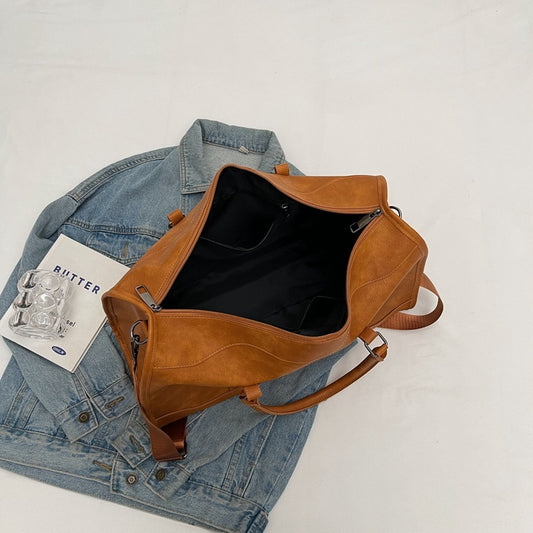 Brown leather bag on a white surface with a denim jacket and magazine underneath.