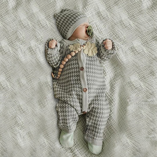 Baby in a knitted outfit with a hat lying on a textured blanket