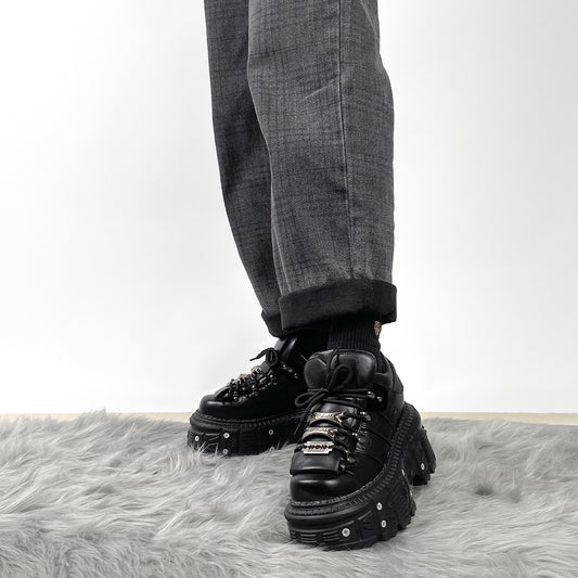Black platform shoes worn with gray pants on a white background