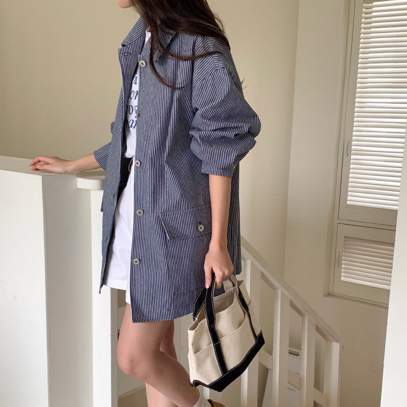 Person wearing a blue striped coat holding a beige handbag indoors.