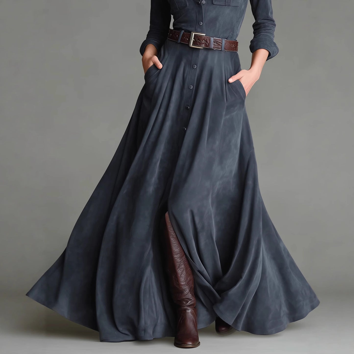 Person wearing a long dark blue dress with brown boots on a gray background