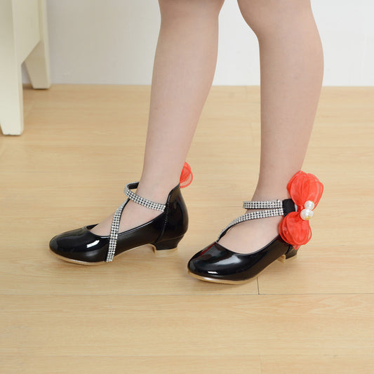 Black shoes with decorative straps and red flowers on a wooden floor.