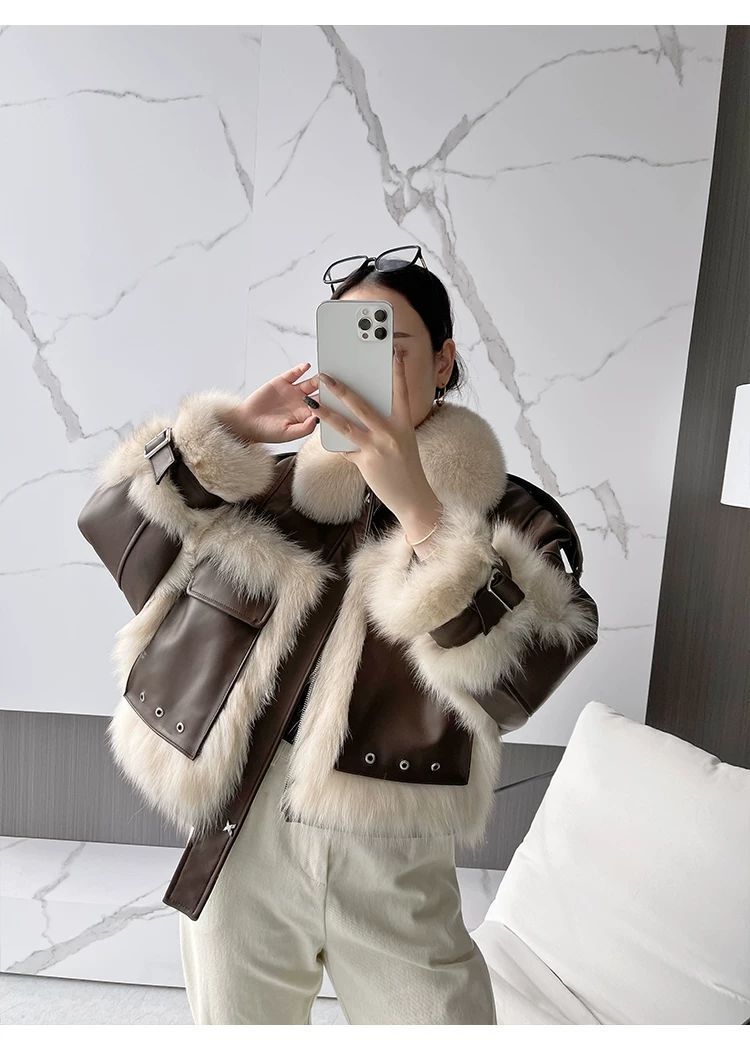 Person wearing a brown leather jacket with white fur trim, taking a mirror selfie.
