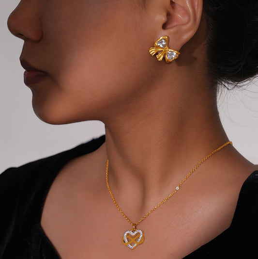 Close-up of a person wearing gold butterfly earrings and a matching necklace with a heart pendant.