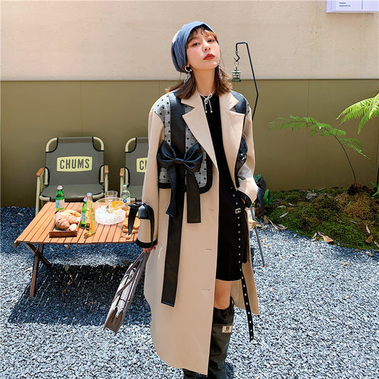 Woman in a long coat standing outdoors with a small table and chairs in the background. by millivan