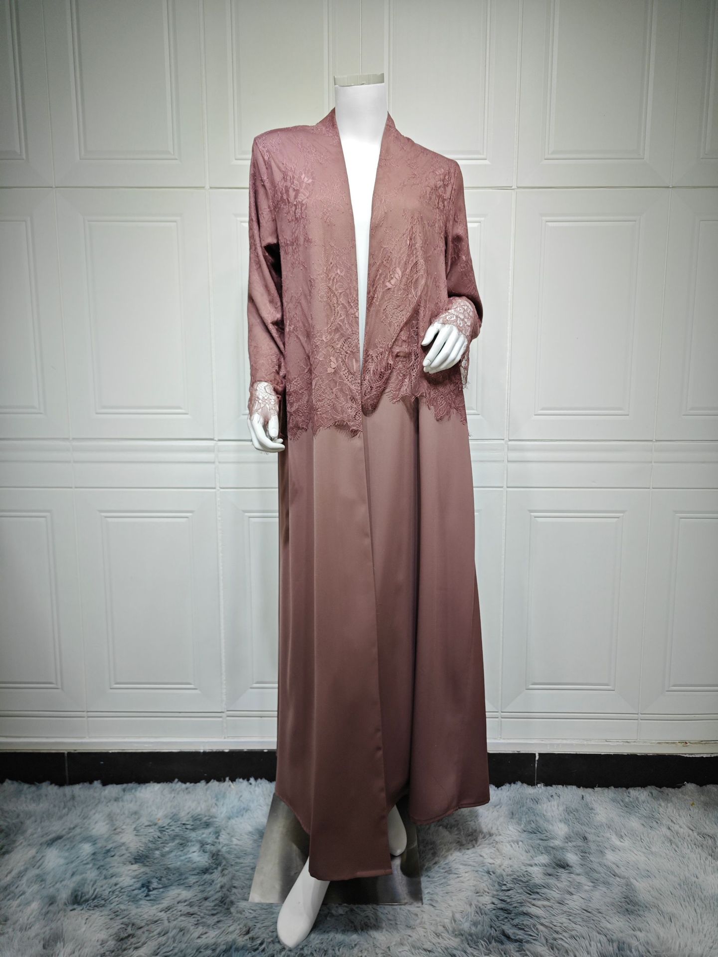 Long brown dress on a mannequin against a white paneled wall.