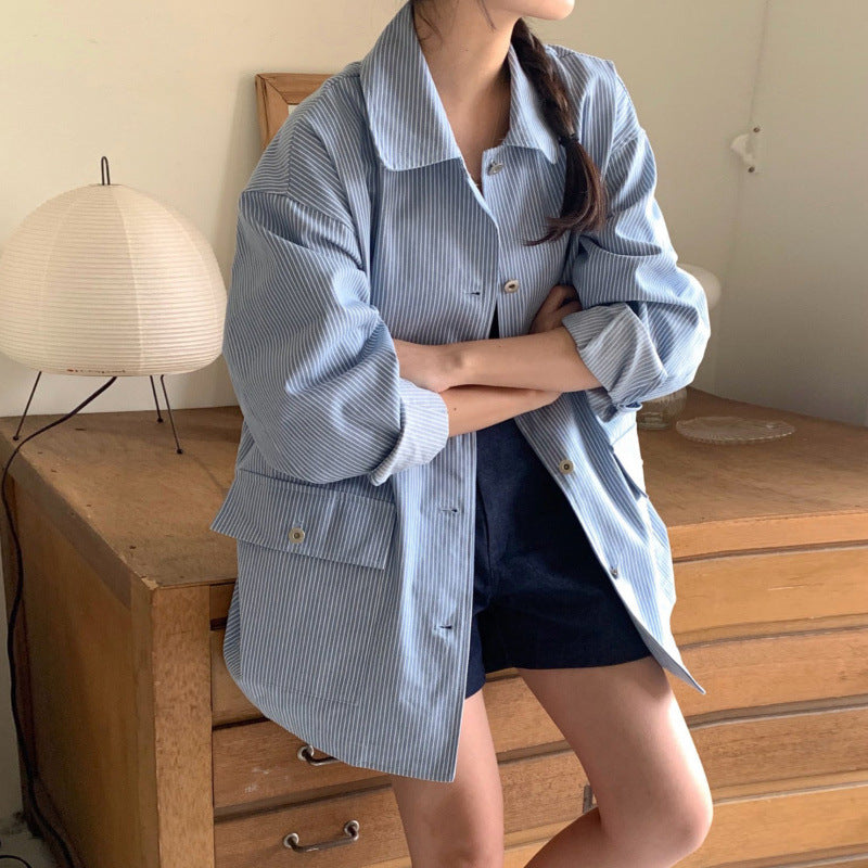 Person wearing a blue striped shirt over a black top with navy shorts, standing in a room with wooden furniture and a lamp.