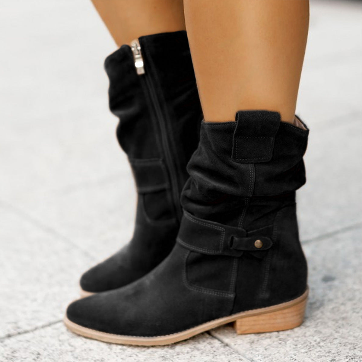 Black knee-high boots with a strap on a light gray background