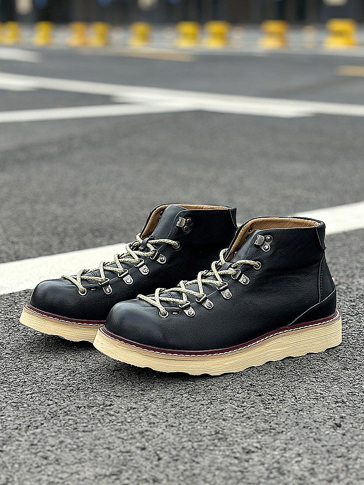 Pair of black leather boots with white soles on a road surface.