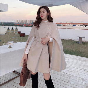 Woman wearing a beige cape coat with a cityscape in the background