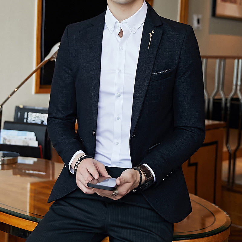 Man in a dark suit and white shirt holding a phone in an indoor setting.