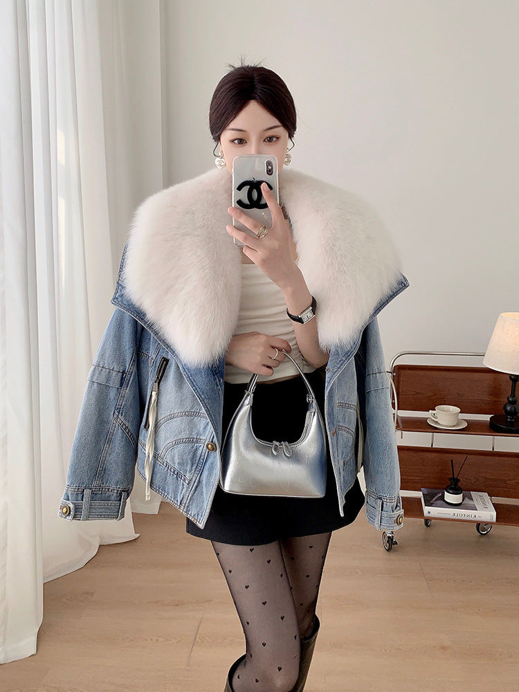 Person wearing a denim jacket with a white fur collar, holding a silver handbag indoors.