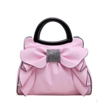 Pink handbag with a large bow and black handle on a white background