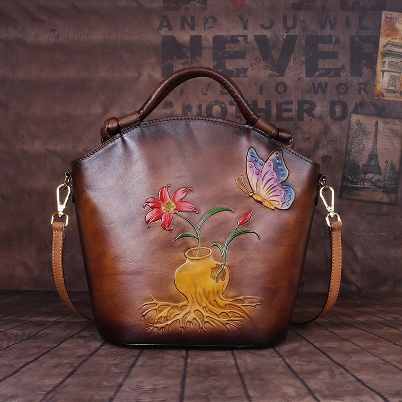 Brown leather handbag with floral and butterfly design on a wooden floor.