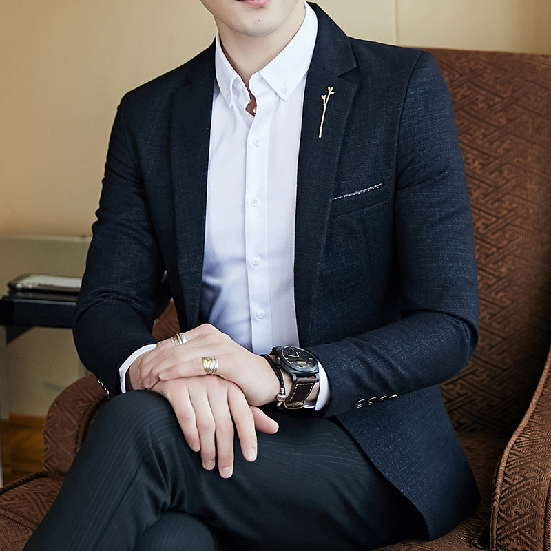 Man wearing a dark suit with a white shirt, sitting on a brown chair.
