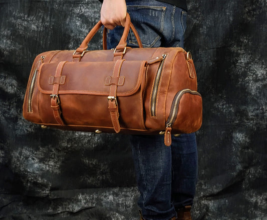 Brown leather duffel bag held by a person against a dark background