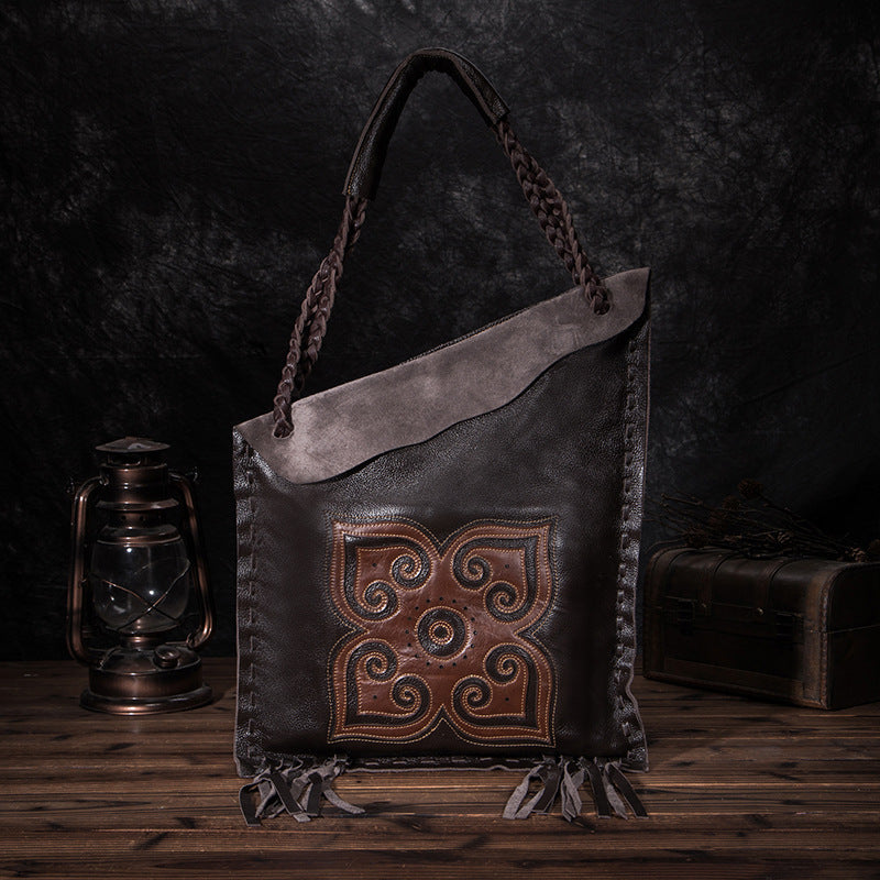 Dark brown leather bag with intricate design on a wooden surface and dark background