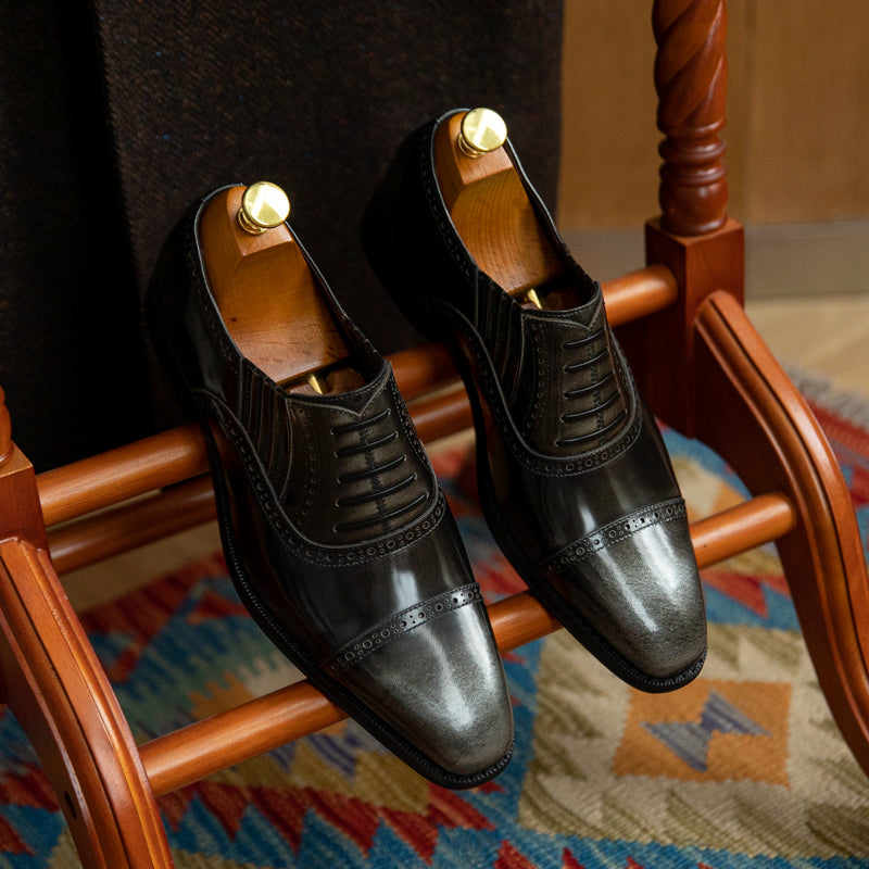 Pair of black dress shoes on a wooden chair with a colorful rug underneath.
