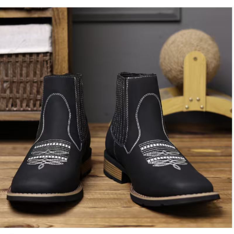 Pair of black leather boots with white stitching on a wooden surface.