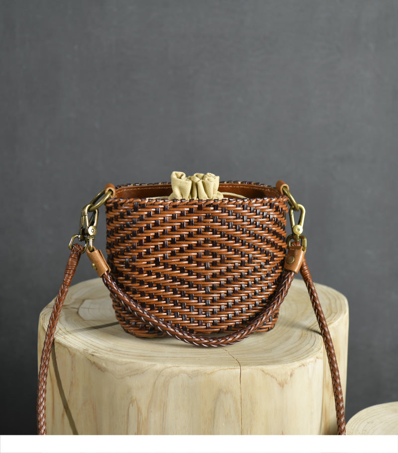 Woven handbag with leather straps on a wooden block against a gray background