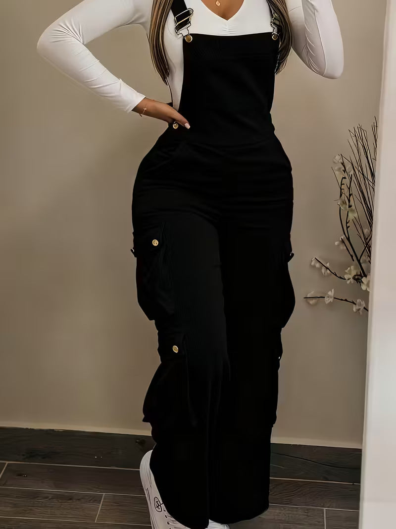Person wearing a black overalls with gold buttons against a neutral wall.