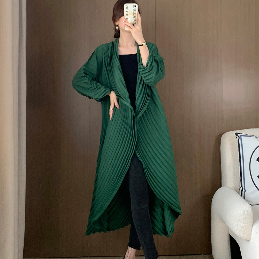 Person wearing a long green coat in a room with a white chair and decorative pillow.