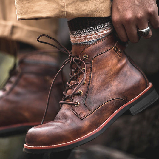 Brown leather boots with laces being tied, worn with a beige jacket and patterned socks.