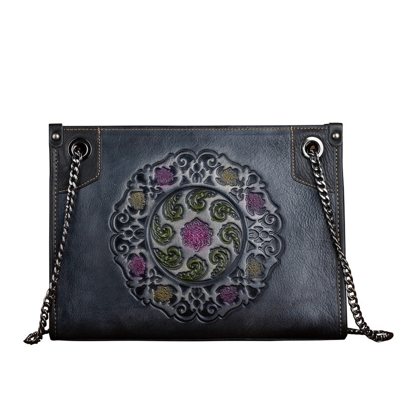 Black leather handbag with floral embossing and chain strap on a white background