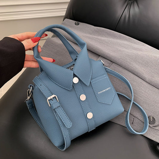 Blue handbag with a collar design held by a hand on a gray surface.