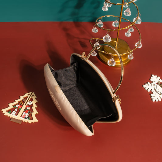 Beige handbag with gold handle on a red surface with Christmas decorations.