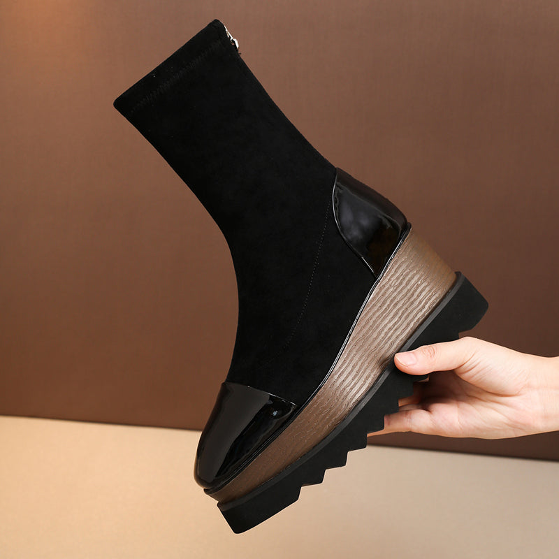 Black sock boot with a wooden sole held by a hand against a brown background