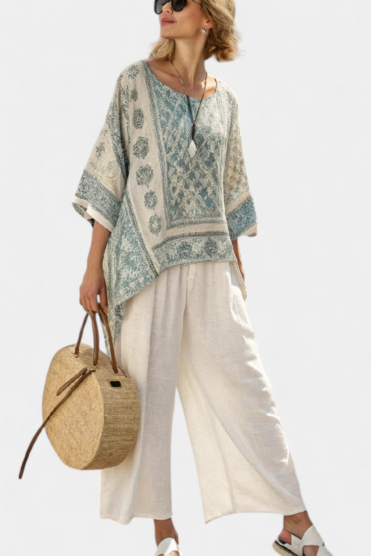 Woman wearing a patterned top and white pants, holding a straw bag on a white background