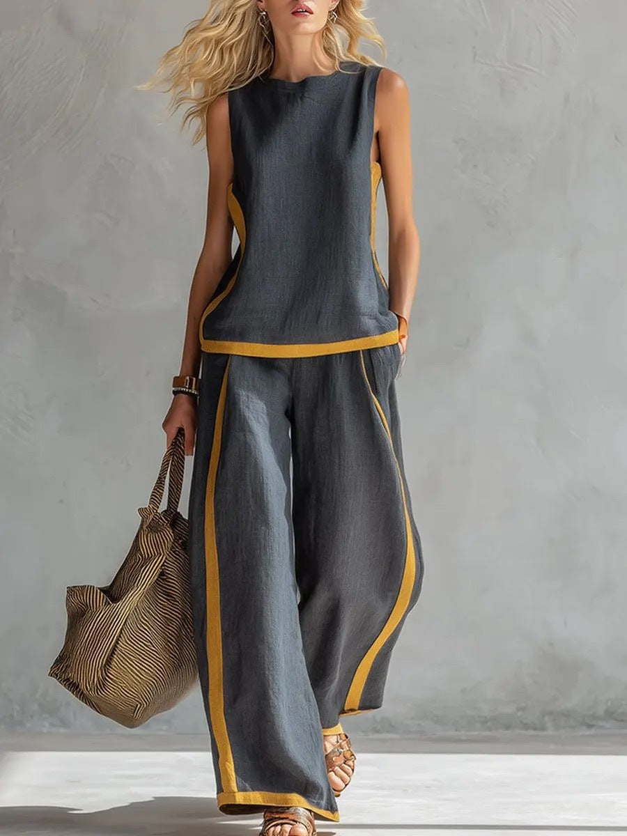 Woman wearing a gray sleeveless top and wide-leg pants with yellow accents, holding a textured bag against a gray background.