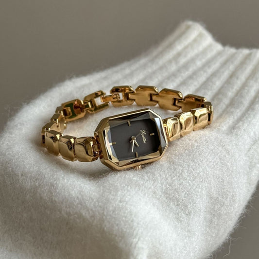 Gold wristwatch with a black face on a white surface